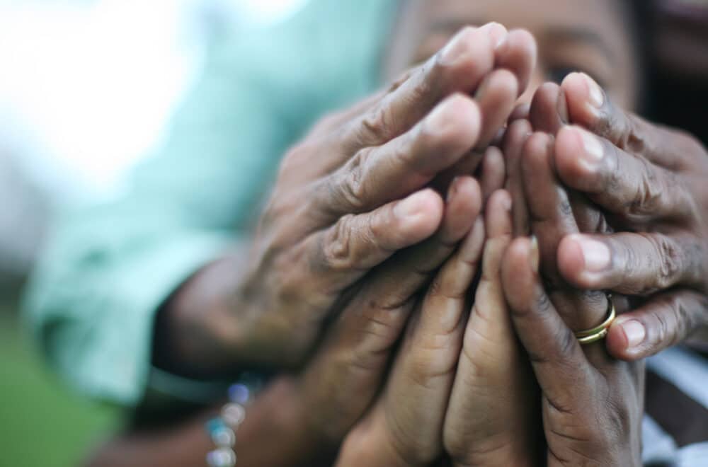 Three pairs of hands that are folded in prayer over eachother in agreement.
