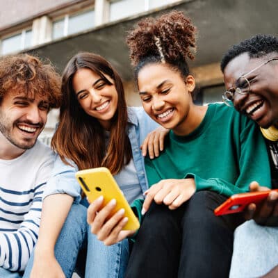 Group of university student friends sitting together using mobile phones to look at discipleship content online.