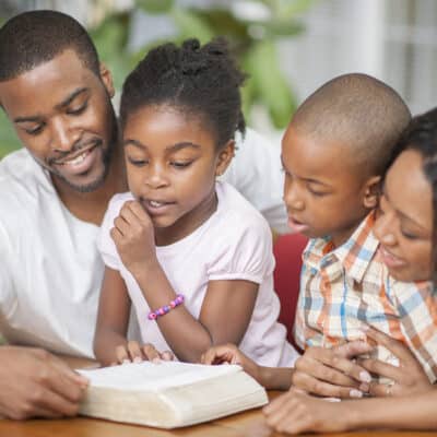 A family of four are sitting together in their home and are reading the Bible together.