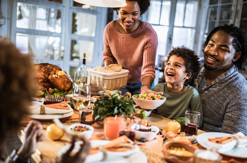 Family laughing and sharing a Thanksgiving meal together at the table.