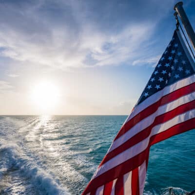 An American flag waves off the back of a boat with the wake from the boat in the ocean behind it.
