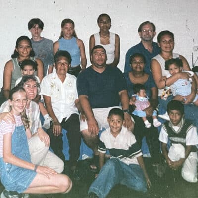 Multi-generational family group gathered indoors, posing together in a living room with adults, children, and babies.