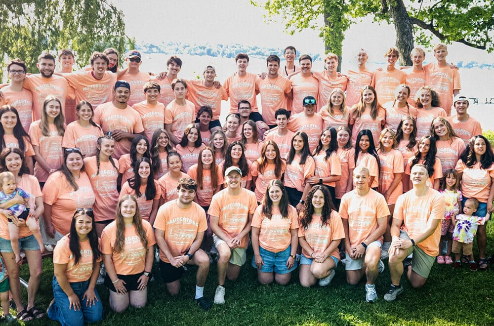 Large group of people wearing peach T-shirts posing outdoors by a lake.